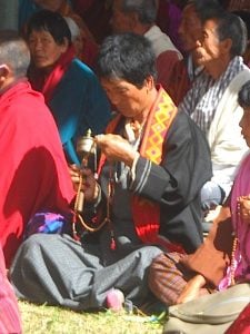 A lay participant says manis (Chenrezig mantra for compassion) on her 108-bead mala while spinning her mani prayer wheel