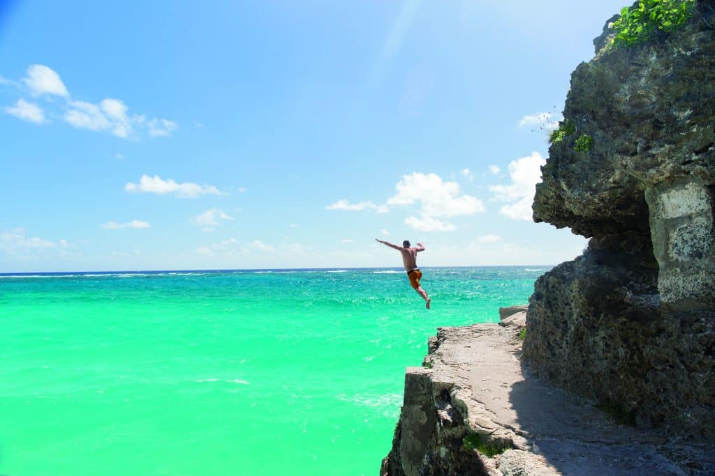 A man jumps off from a cliff into green emerald waters - a representative pic to denote cruise holidays and the flash discounts you can avail to have deals like these