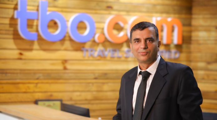 ITTN Exclusively Chats to Neeraj Gera, President of TBO, which Recently Acquired Bookabed Neeraj Gera in a black suit and tie, and in the background is a wooden wall with the words tbo.com
