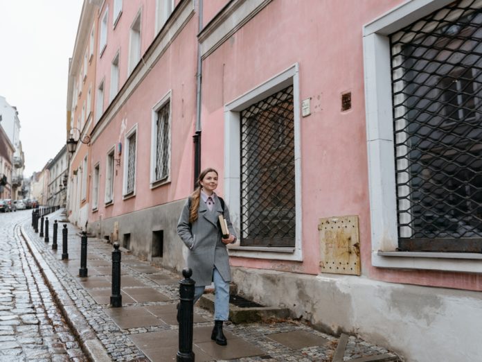 A woman in an overcoat walks on a pavement in Europe